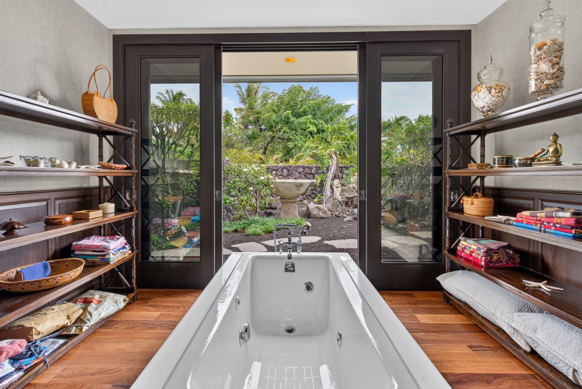 Luxury soaking tub framed by dark wood shelving and a tropical garden view