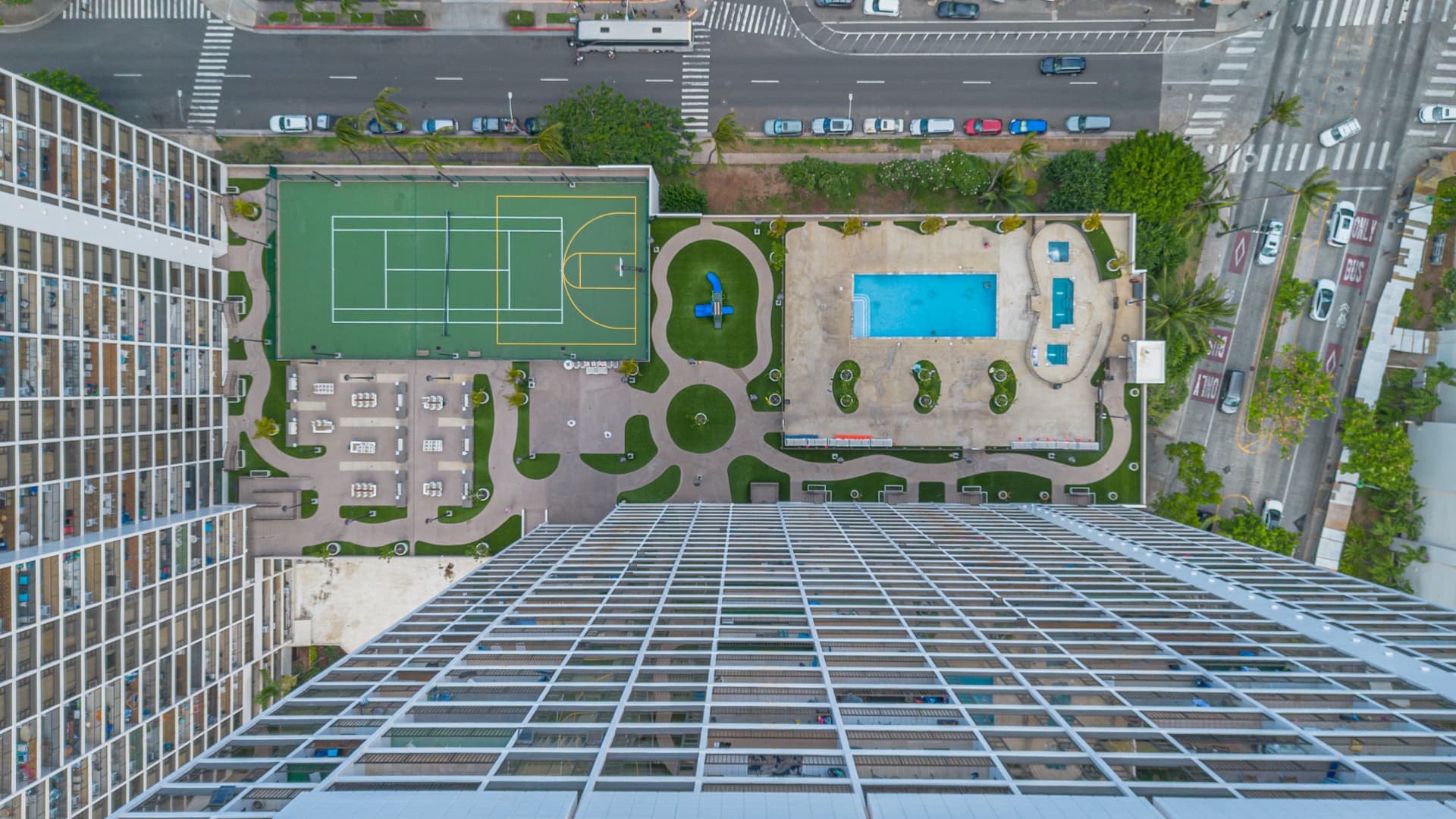 Top-down drone view of a residential pool, courts, lawns, and recreation areas